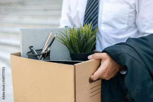 Businessman with box cardboard packing personal items after losing jobs. Failure businessman standing at front of building. Your fired Unemployed Jobless People Crisis photo