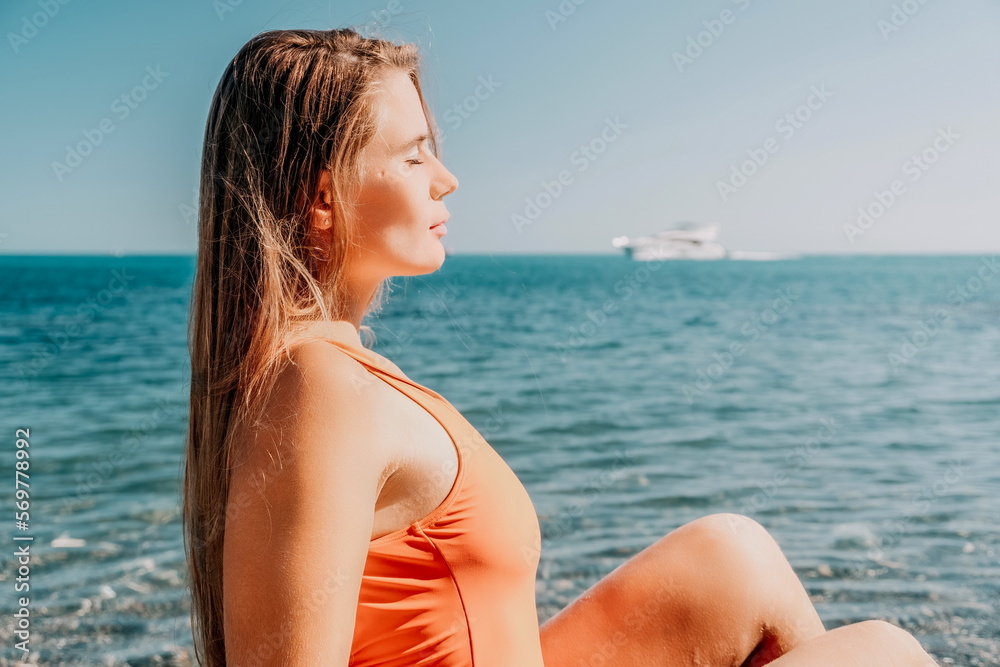 Young woman in red bikini on Beach. Girl lying on pebble beach and enjoying sun. Happy lady with long hair in bathing suit chilling and sunbathing by turquoise sea ocean on hot summer day. Close up