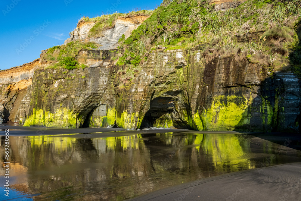 Reflections of green-coloured cliffs on the low-tidal beach