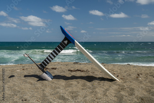 A kitesurfing hydrofoil board on a beach with turquoise sea and waves behind, blue sky with clouds. photo