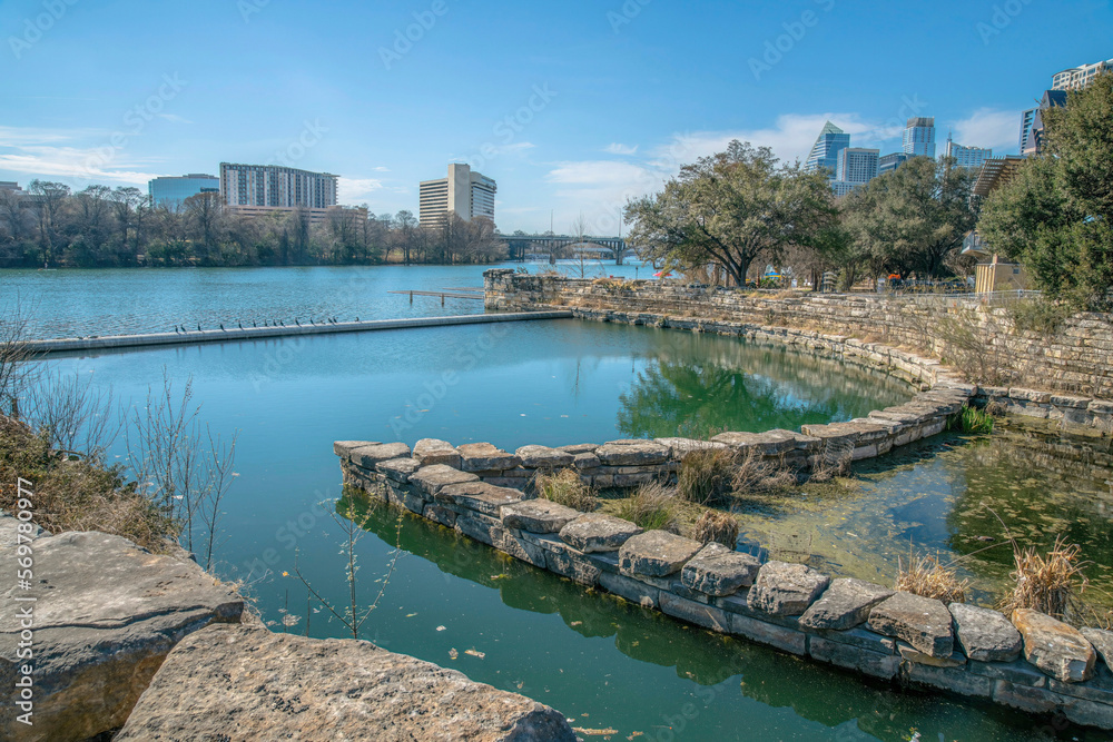 Boat launch ramp with green waters from Colorado River at Austin, Texas. Boat ramp with large stones on sides with views of multi-storey buildings across against the blue skies.