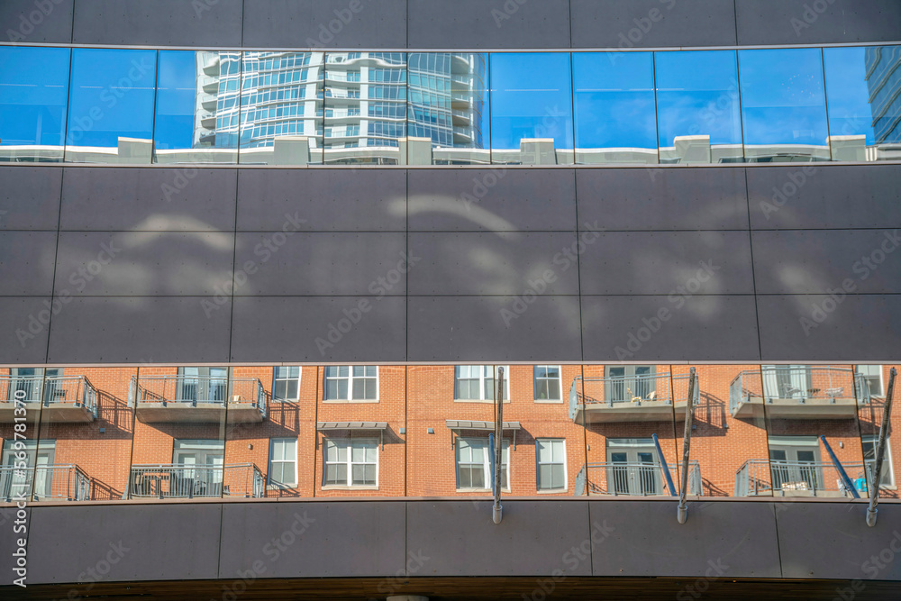 Building exterior with painted concrete slab and reflective glass wall panels at Austin, Texas. Building wall with reflections of residential buildings across from the mirror like glass wall cladding. Building exterior with painted concrete slab and reflective glass wall panels at Austin, Texas. Building wall with reflections of residential buildings across from the mirror like glass wall cladding.