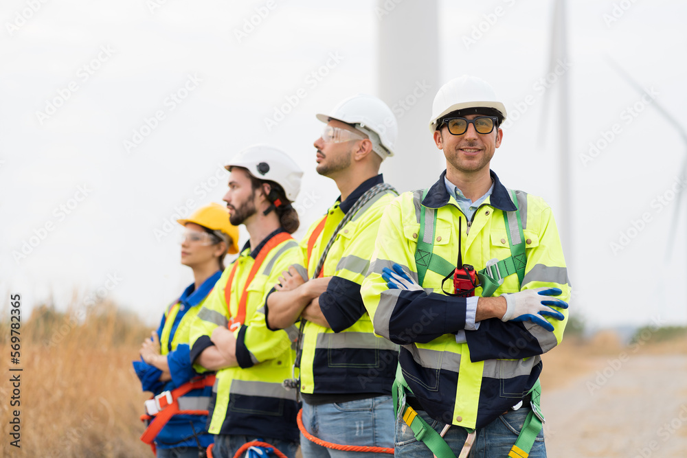Portrait of group male and female engineers wear safety uniform and equipment preparing plan inspecting or maintenance of wind turbines at wind farm. Team of engineers working at wind turbines farm Portrait of group male and female engineers wear safety uniform and equipment preparing plan inspecting or maintenance of wind turbines at wind farm. Team of engineers working at wind turbines farm