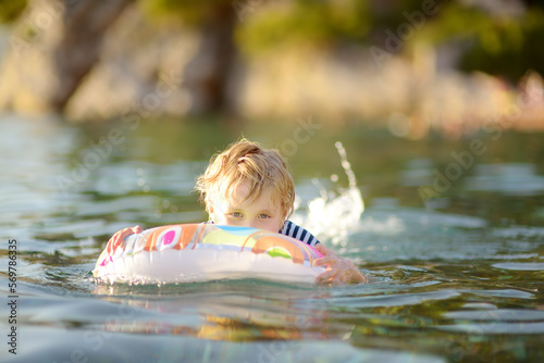 Fototapeta Naklejka Na Ścianę i Meble -  Little boy swimming with colorful floating ring in sea on sunny summer day. Cute child playing in clean water. Family and kids resort holiday during summer vacations.