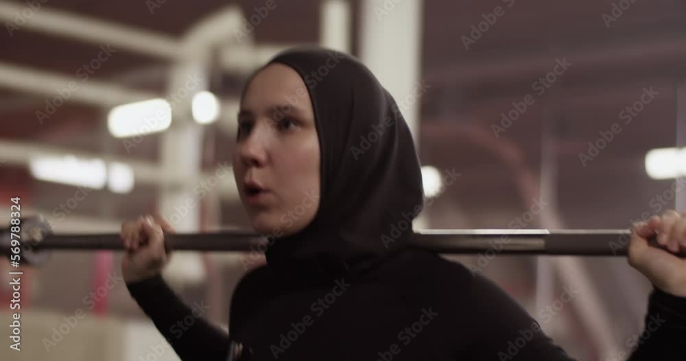 Determined Muslim sportswoman exercising with barbell