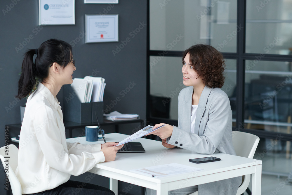 Obraz premium Young candidate showing her resume to manager while they sitting at table and talking at job interview