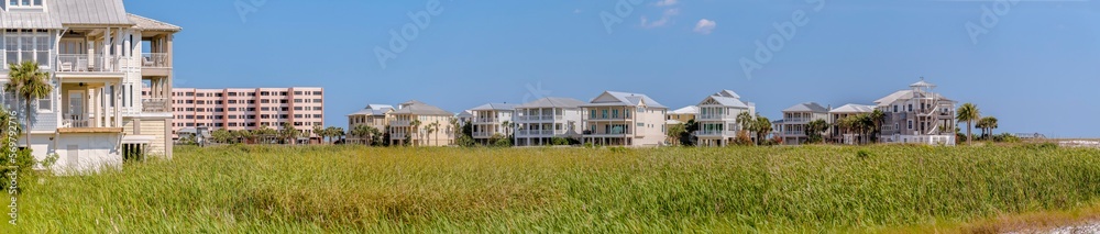 Homes on the beach in panorama at Destin point in Destin, Florida. There are tall green grasses at the front of three-storey houses and multi-storey apartment on the left. Homes on the beach in panorama at Destin point in Destin, Florida. There are tall green grasses at the front of three-storey houses and multi-storey apartment on the left.