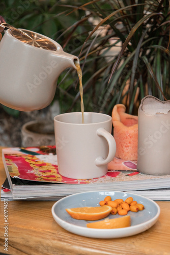  Black fruit tea with sea buckthorn and orange on a wooden table in a cafe candlelight dinner is poured into a gray mug