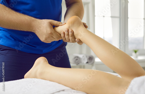 Crop close up of male masseur massage patient foot relieve strain or spasm in muscles. Therapist work with customer leg recovery in wellness clinic. Rehabilitation and body care treatment concept.