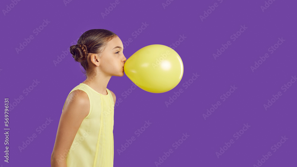 Cheerful funny little girl inflates yellow balloon isolated on vivid purple background. Profile portrait of cute preteen girl who inflates balloon near copy space. Children's holidays concept. Banner. Cheerful funny little girl inflates yellow balloon isolated on vivid purple background. Profile portrait of cute preteen girl who inflates balloon near copy space. Children's holidays concept. Banner.