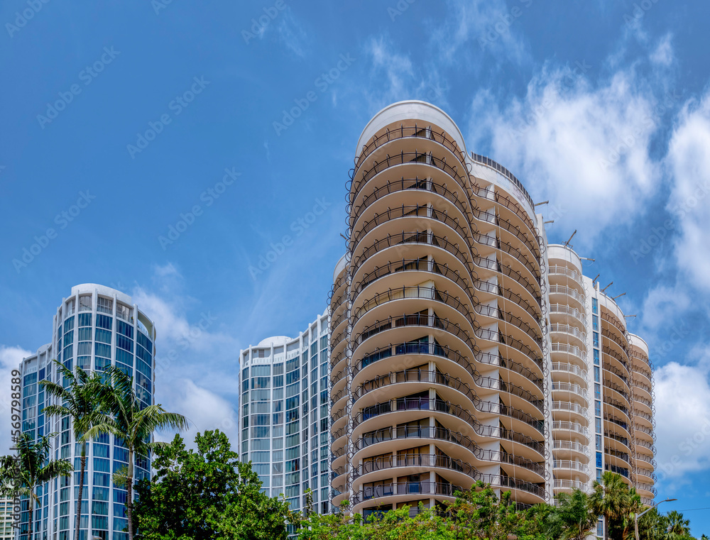 Modern residential buildings against the blue sky with clouds background. There are trees at the front of the multi-storey residential buildings with modern exterior.
