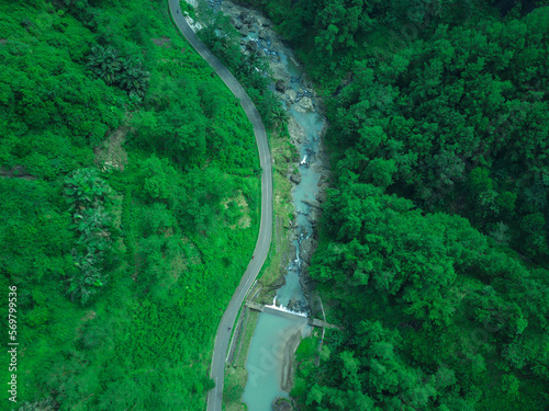 Aerial view of Indonesia's aesthetic highway squeezed by 2 hills and flowed by a stunning river © mafifp-id