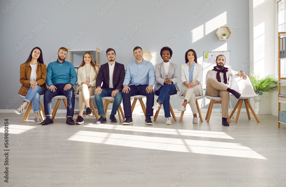 Fototapeta premium Human resource. Confident smiling multiracial professional business people of all ages sit on chairs in a row. Group portrait of happy job candidates looking at camera while sitting in light office
