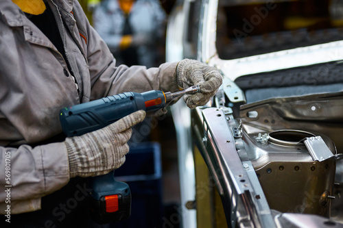 Worker prepares to screw car body parts on workshop conveyor