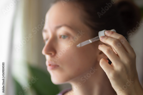 Young woman using facial vitamin serum or essential oil with pipette, applying on face. Skincare and face care concept.