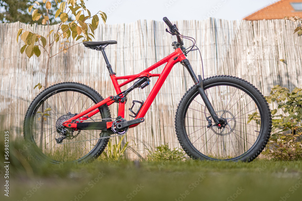 Side view of a modern mountain bike or bicycle for off road. Enuduro mtb bicycle parked on a lawn. Red MTB standing upright on grass, static, no people.