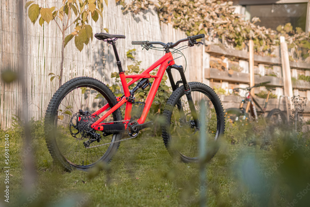 Side view of a modern mountain bike or bicycle for off road. Enuduro mtb bicycle parked on a lawn. Red MTB standing upright on grass, static, no people. Side view of a modern mountain bike or bicycle for off road. Enuduro mtb bicycle parked on a lawn. Red MTB standing upright on grass, static, no people.