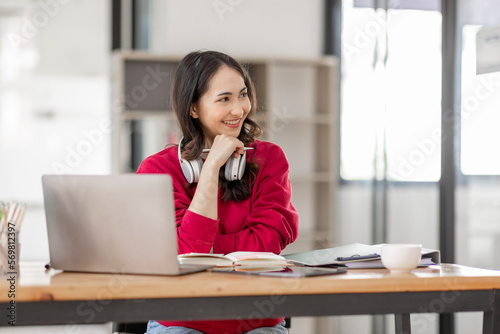 Portrait of Young asian woman wearing headphones using laptop in cafe, writing notes, learning language, watching online business or education concept