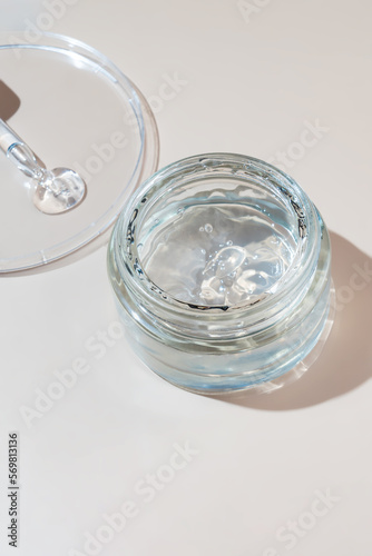 Jar with transparent cosmetic product, aloe gel or creamgel on beige pastel background. Liquid gel spilled out of cosmetic pipette on petri dish. Unbranded packaging, copy space.