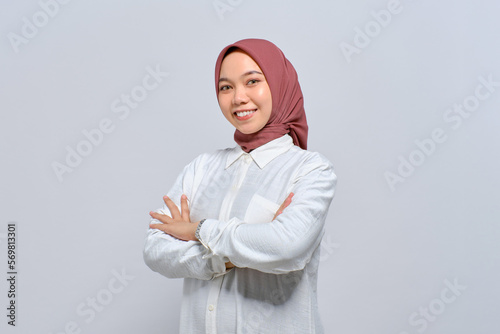 Smiling young Asian Muslim woman standing with crossed arms and looking confident isolated over white background
