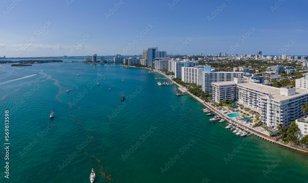 Intracoastal buildings in an aerial view at Miami Beach, Florida. Waterfront with boats and harbors at the front of some buildings on the right side and background of clear blue skyline.
