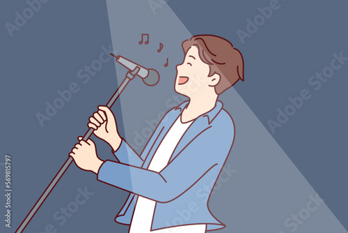 Man pop star sings song leaning back with microphone on tripod in hands during performance at concert. Happy guy performs popular song for own fans while standing in spotlight