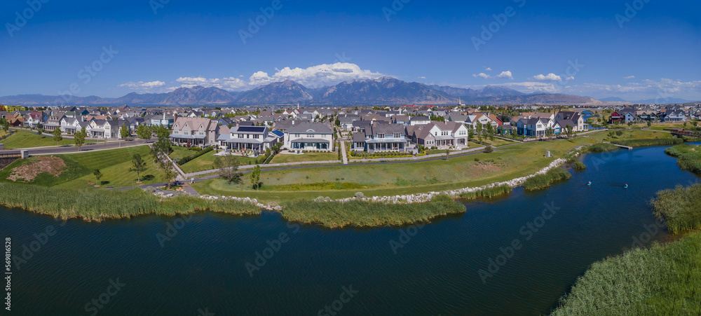Beautiful houses in Daybreak Utah with view of river in the foreground. Magnificent mountains, blue sky, and clouds can be seen in the background of the neighborhood.