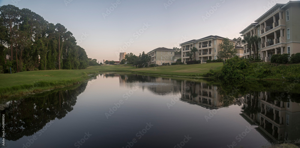 Lake with reflections of the residential buildings near the shore at Destin, Florida. Three-storey residential buildings with balconies and lakefront views with grass and trees on the shore.