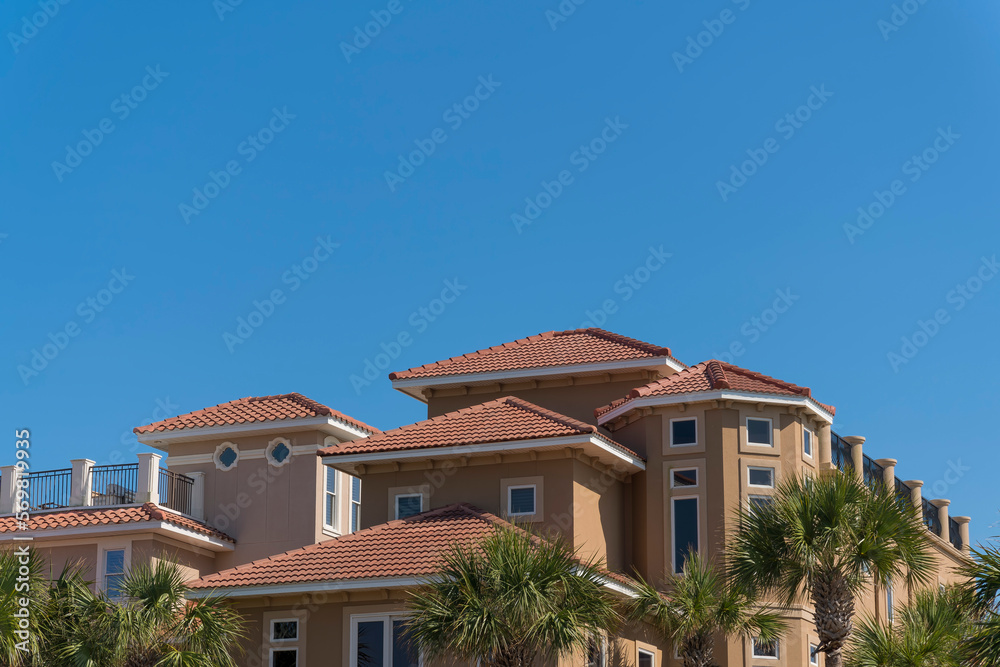 Two large residential buildings with railings on roof decks in Destin, Florida. There are palm trees outside the mansions villas against the clear blue sky. Two large residential buildings with railings on roof decks in Destin, Florida. There are palm trees outside the mansions villas against the clear blue sky.