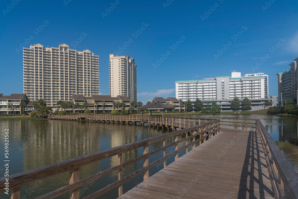 Wooden boardwalk with railings with views of modern high rise buildings in Destin, Florida. Wooden walkway over the reflective water near the city buildings