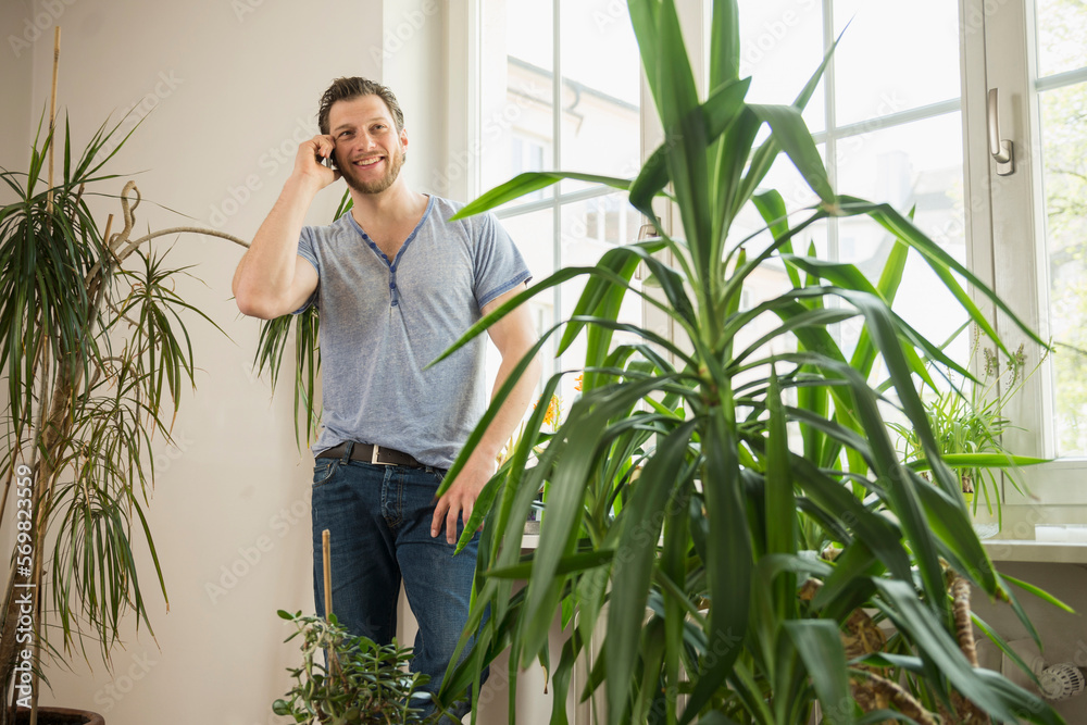 Mid adult man talking on mobile phone in living room and smiling, Munich, Bavaria, Germany Mid adult man talking on mobile phone in living room and smiling, Munich, Bavaria, Germany