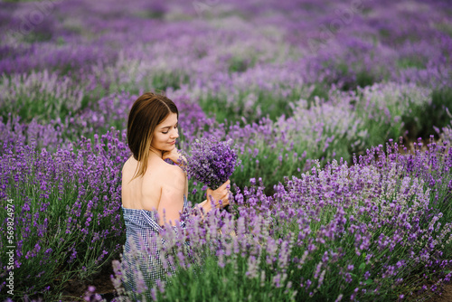 Beautiful girl in a dress in purple lavender field. Woman walking on the lavender field. Female collects lavender. Enjoy the floral glade, and summer nature. Natural cosmetics and eco makeup concept.