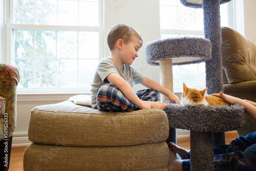 Happy Young Boy Sits Smiling and Playing with Resting Pet Cat photo