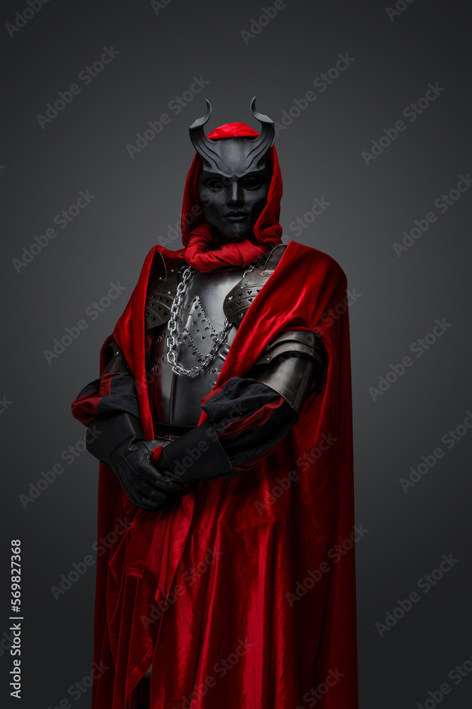 Portrait of dark knight with red robe and black mask isolated on gray background.