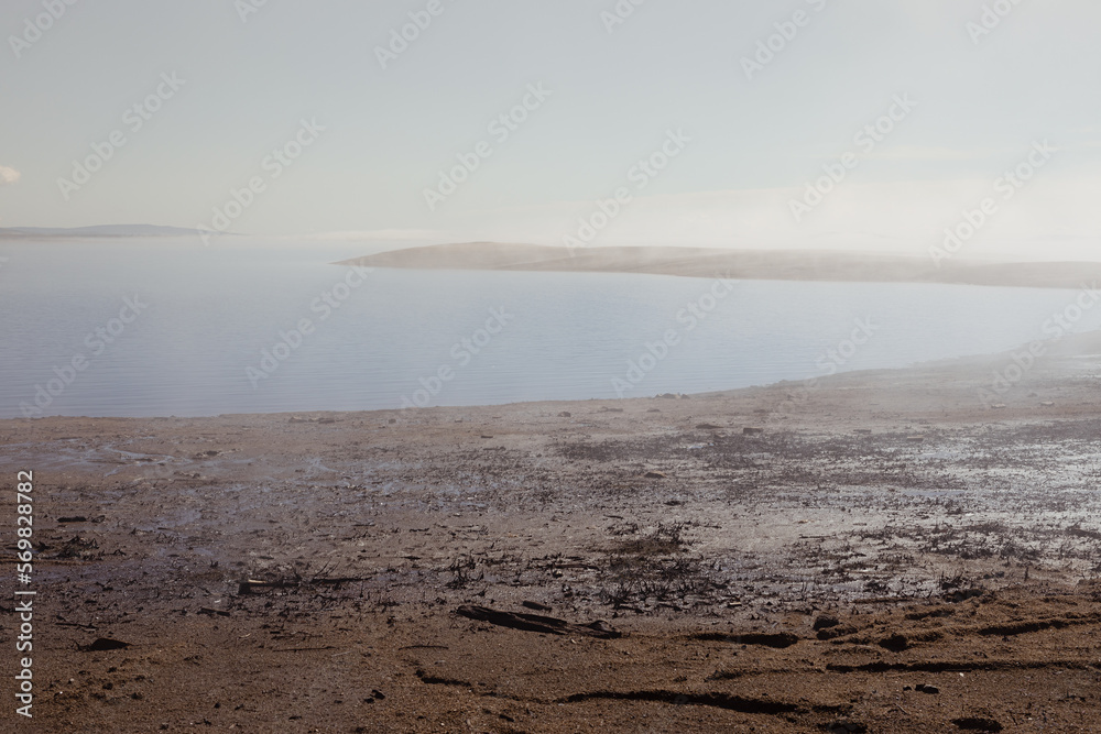 Atmospheric empty sea shore in early morning with fog above quiet water and sunlight on horizon with pebble beach and cape in haze. Zen and meditative landscape. Atmospheric empty sea shore in early morning with fog above quiet water and sunlight on horizon with pebble beach and cape in haze. Zen and meditative landscape.