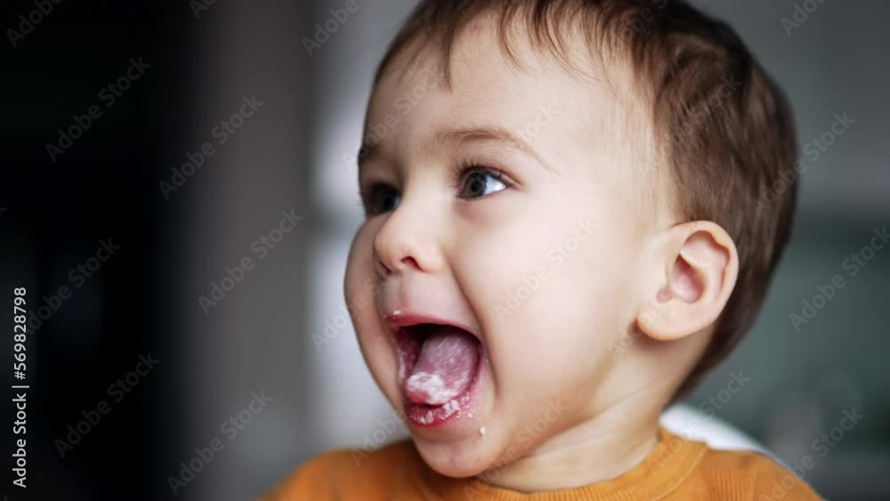 Lovely little child being naughty during feeding. Boy opens smudged mouth, showing his tongue. Close up. Lovely little child being naughty during feeding. Boy opens smudged mouth, showing his tongue. Close up.