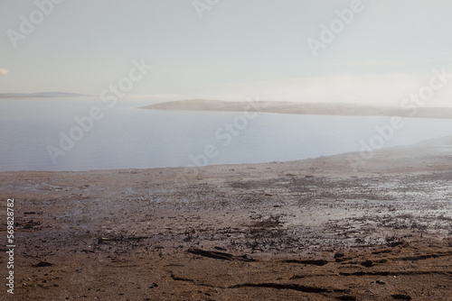 Atmospheric empty sea shore in early morning with fog above quiet water and sunlight on horizon with pebble beach and cape in haze. Zen and meditative landscape.