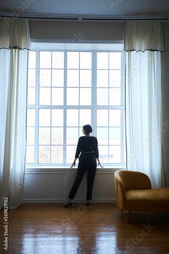 A beautiful woman is standing at a large window
