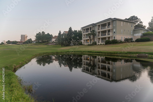 Golf course with reflective pond against sky during sunset in Destin Florida. The multi-storey building with balconies is reflected in the calm water. © Jason