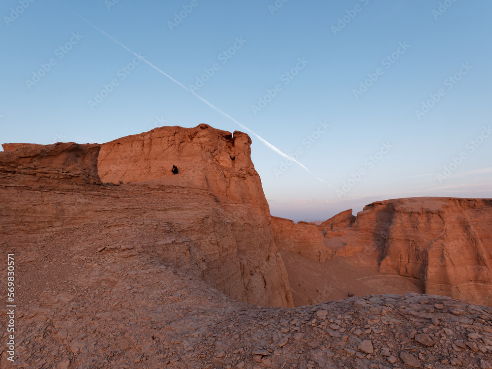 Serene sunset over the amazing Dasht-e Lut Desert and its rock formations (Kaluts) at sunset and silhouette of a man standing on the rock, Kerman Province, Iran