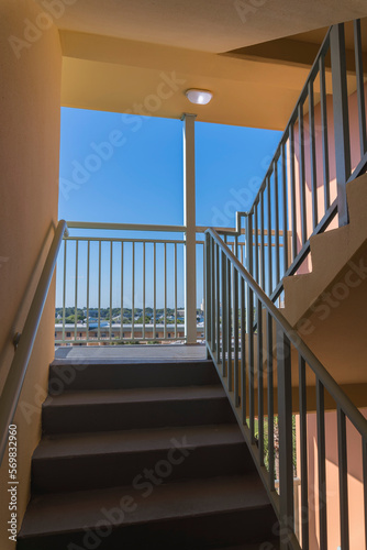 Stairwell with natural daylight from a landing with railings and outside views at Destin, Florida. Building interior open-air stairwell with wall-mounted handrail and concrete steps and landing. photo