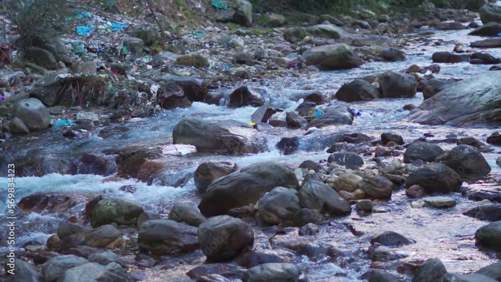 Closeup shot of river Parvati flowing in between mountains at Kasol with plastic waste around the river with some plastic waste floating in the stream. Waste dumped on side of river in Himachal. Closeup shot of river Parvati flowing in between mountains at Kasol with plastic waste around the river with some plastic waste floating in the stream. Waste dumped on side of river in Himachal.
