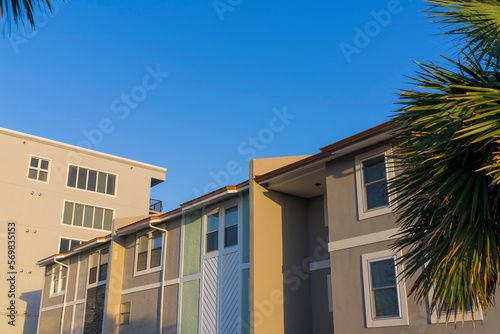 Exterior view of home on a sunny day in Destin Florida residential neighborhood. The houses has small glass paned windows and sunlit walls against clear blue sky and trees.