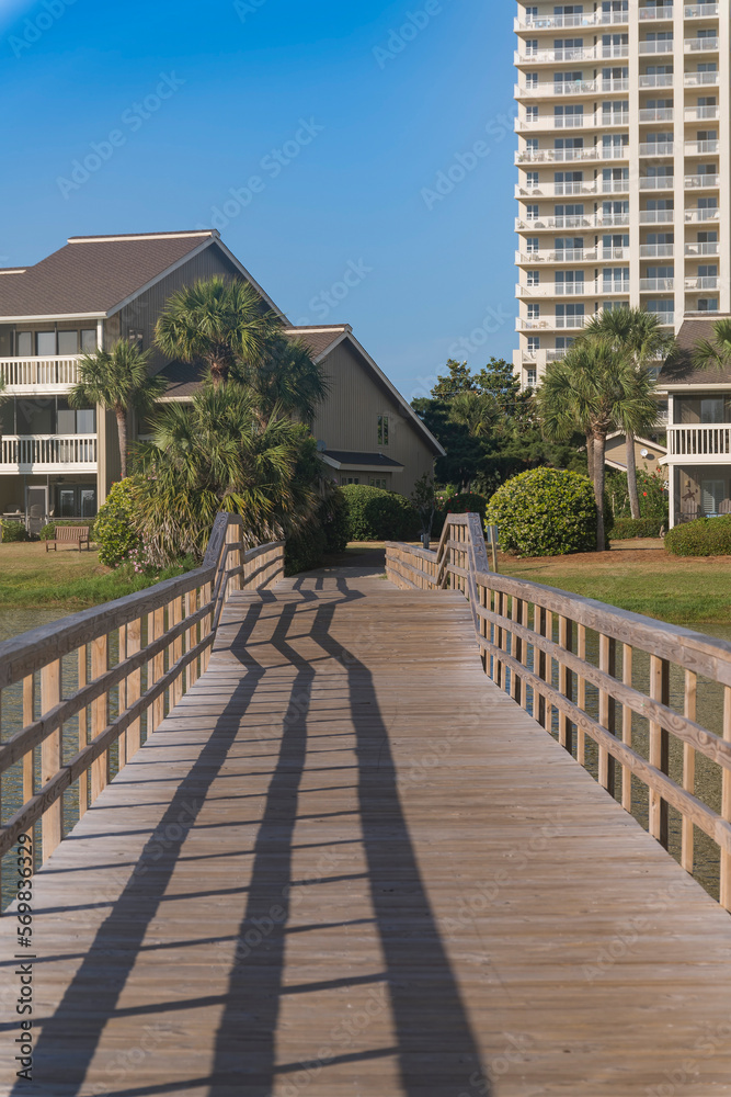 Wooden boardwalk with an arched bridge heading to the apartments in Destin, Florida. Pathway over the lake at the front of residential area.