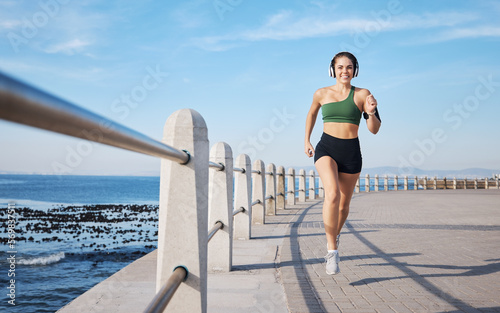 Running, music and woman at beach for fitness, exercise and morning cardio with energy in sports. Radio, podcast and workout run by girl at ocean for training, happy or relax with audio motivation