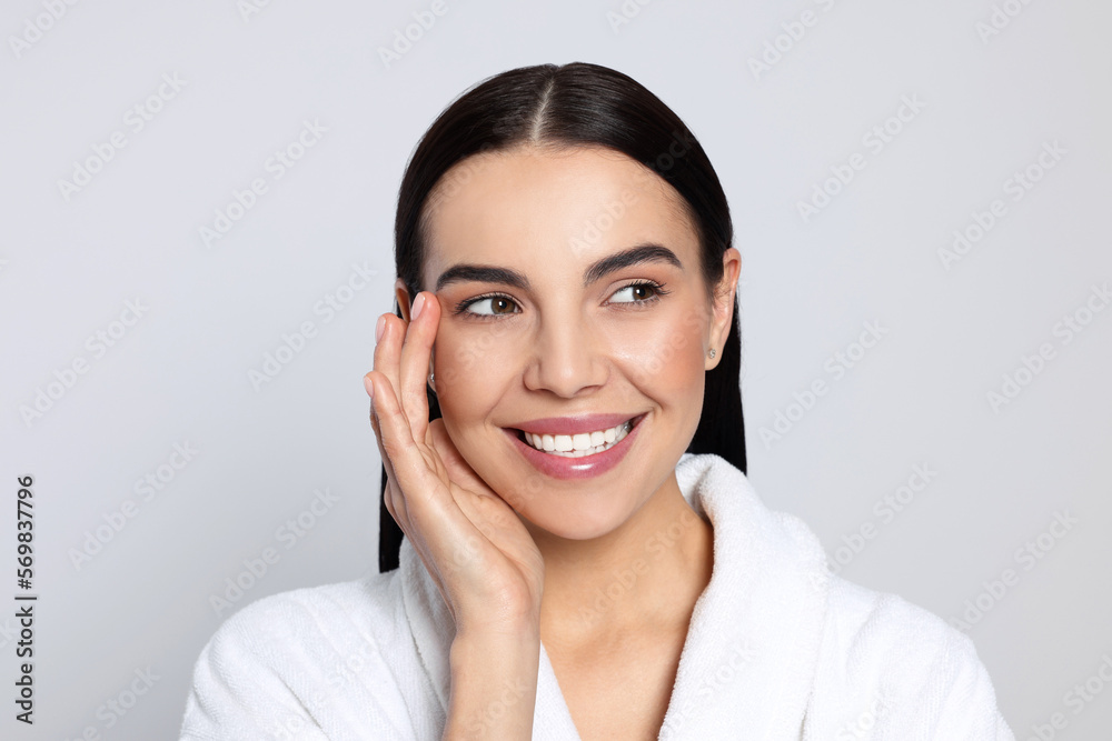 Portrait of attractive young woman in bathrobe on light grey background. Spa treatment Portrait of attractive young woman in bathrobe on light grey background. Spa treatment