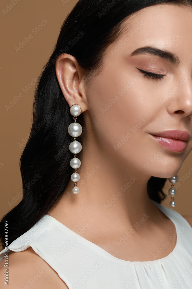 Young woman wearing elegant pearl earrings on brown background, closeup