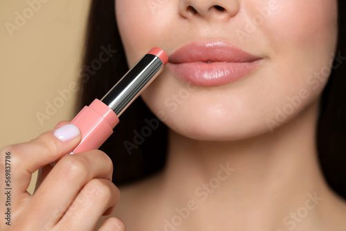 Young woman applying nude lipstick on beige background, closeup © New Africa