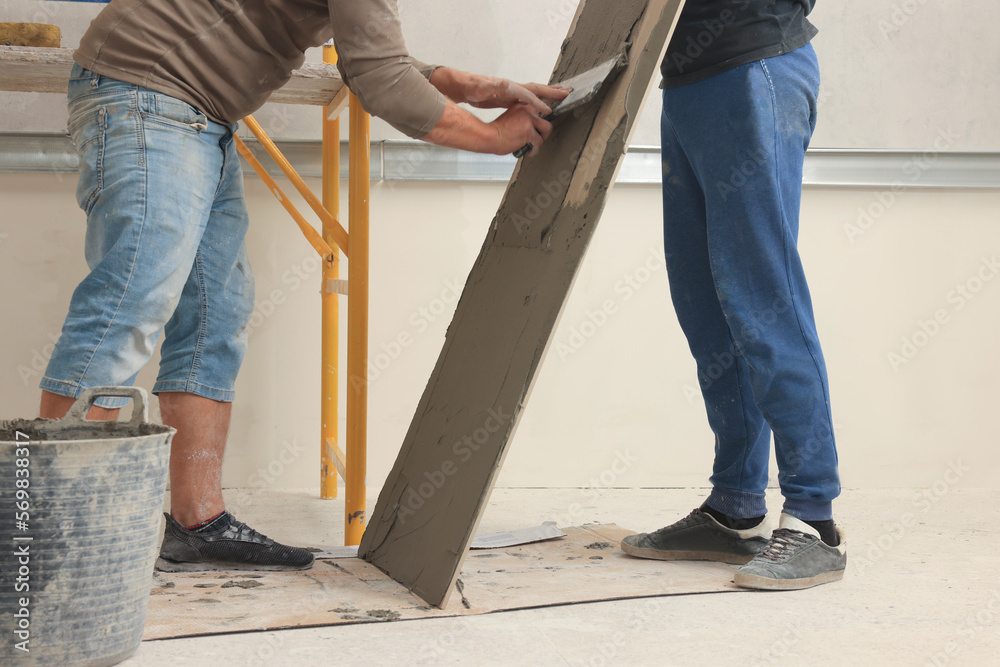 Worker spreading adhesive mix over tile with spatula, closeup Worker spreading adhesive mix over tile with spatula, closeup