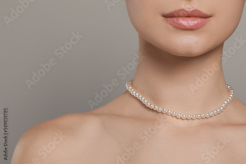 Young woman wearing elegant pearl necklace on grey background, closeup. Space for text